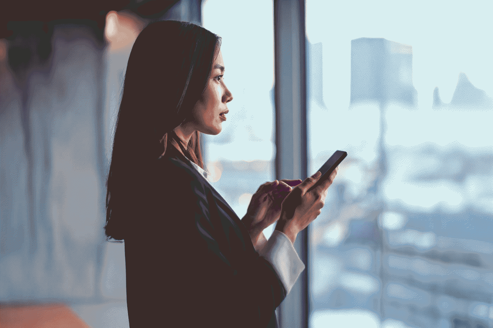 Une professionnelle consulte son smartphone devant la baie vitrée d’un immeuble de bureaux